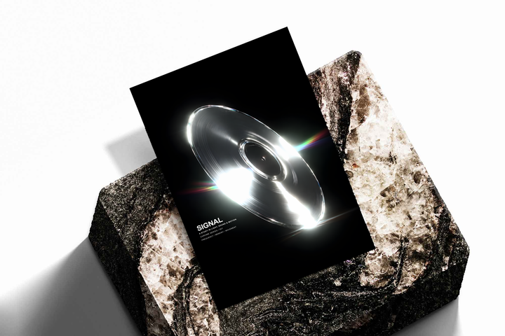 SIGNAL music graphic with a reflective silver grooved disc, white highlights and rainbow streaks on black, shown as an unframed print tilted on a dark stone display against a light background