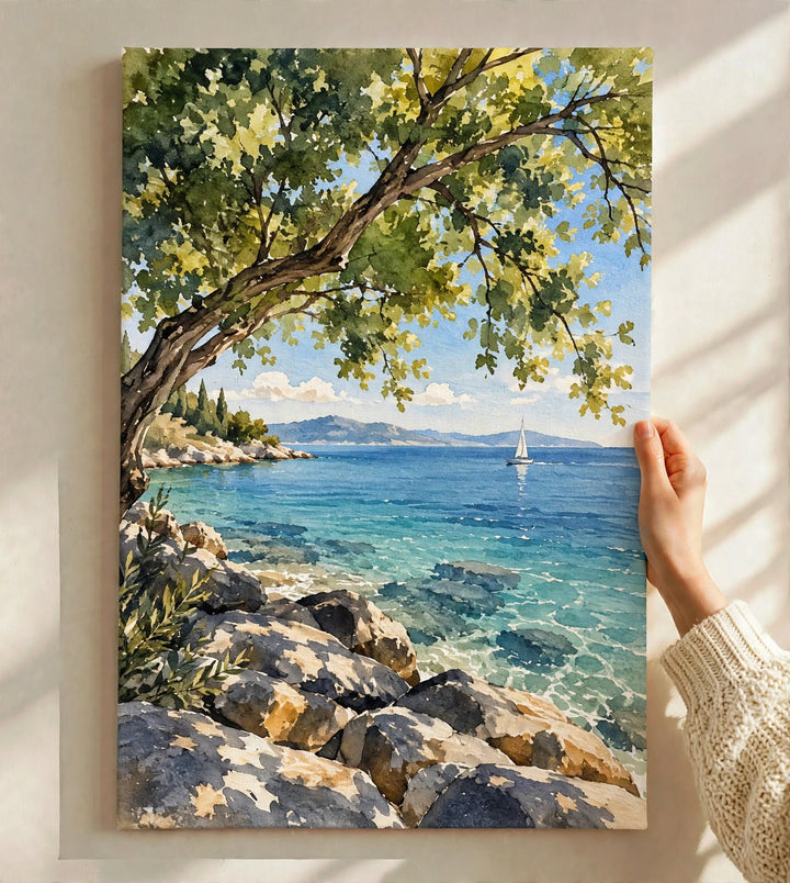 Mediterranean Coast Watercolor Art Print held against a softly lit wall with a tranquil seaside view framed by green foliage