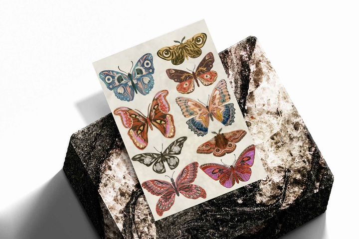 Unframed artwork depicting symmetrical arrangement of colorful butterflies and moths, presented diagonally on rough stone.