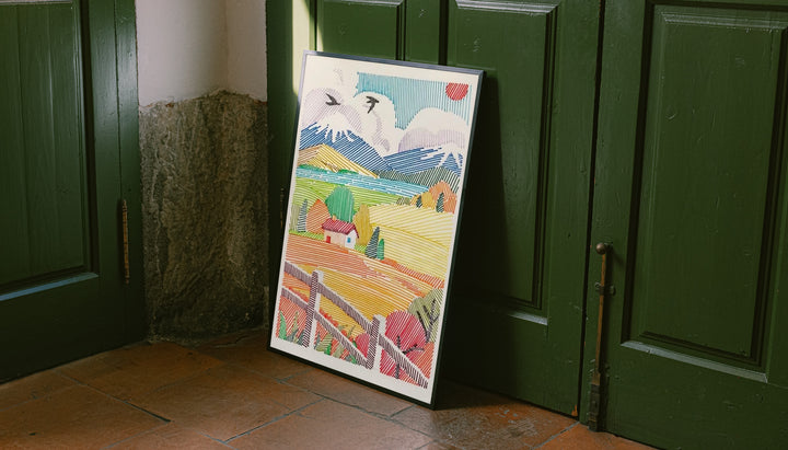 A red-roof farmhouse among colorful striped fields, mountains, birds and a foreground fence leaning on the floor against dark green wall panelling