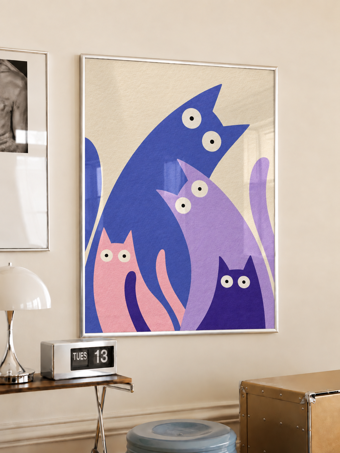 White-framed colourful four-cat poster hanging above a wooden side table in a warm neutral room.