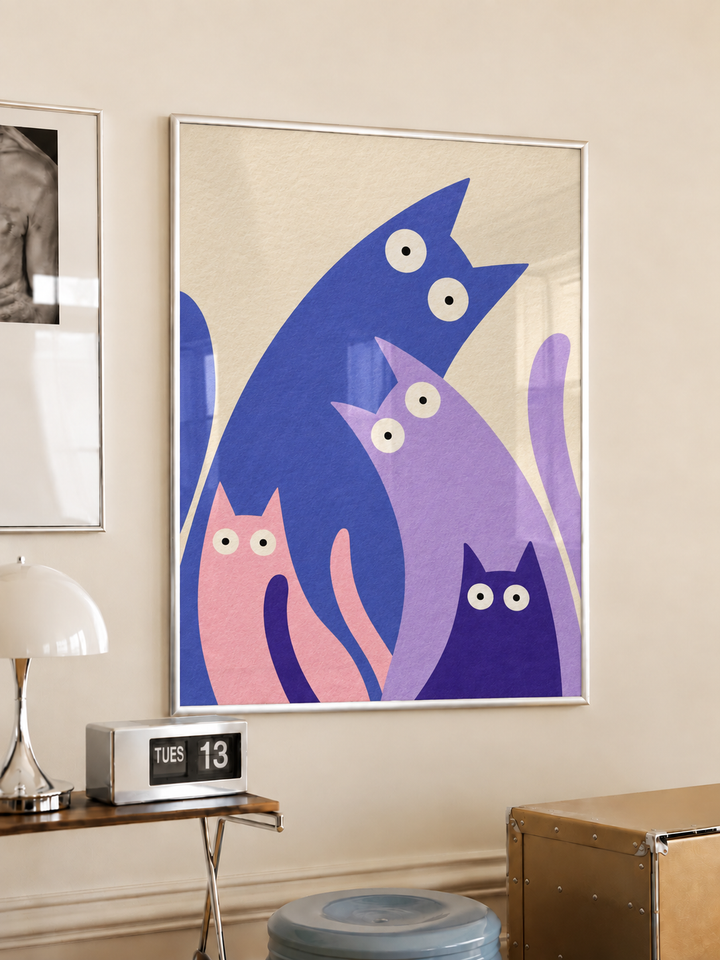 White-framed colourful four-cat poster hanging above a wooden side table in a warm neutral room.