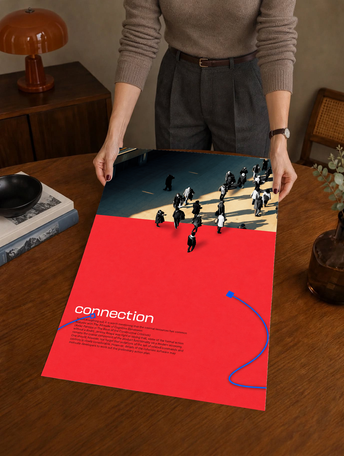 Street pedestrians above a red field with Connection text and two blue cable shapes as a large unframed poster held above a wooden desk