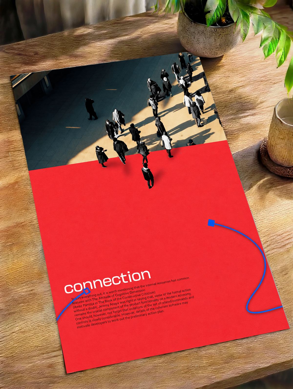 Street pedestrians above a red field with Connection text and two blue cable shapes as an unframed poster lying on a wooden table beside a plant