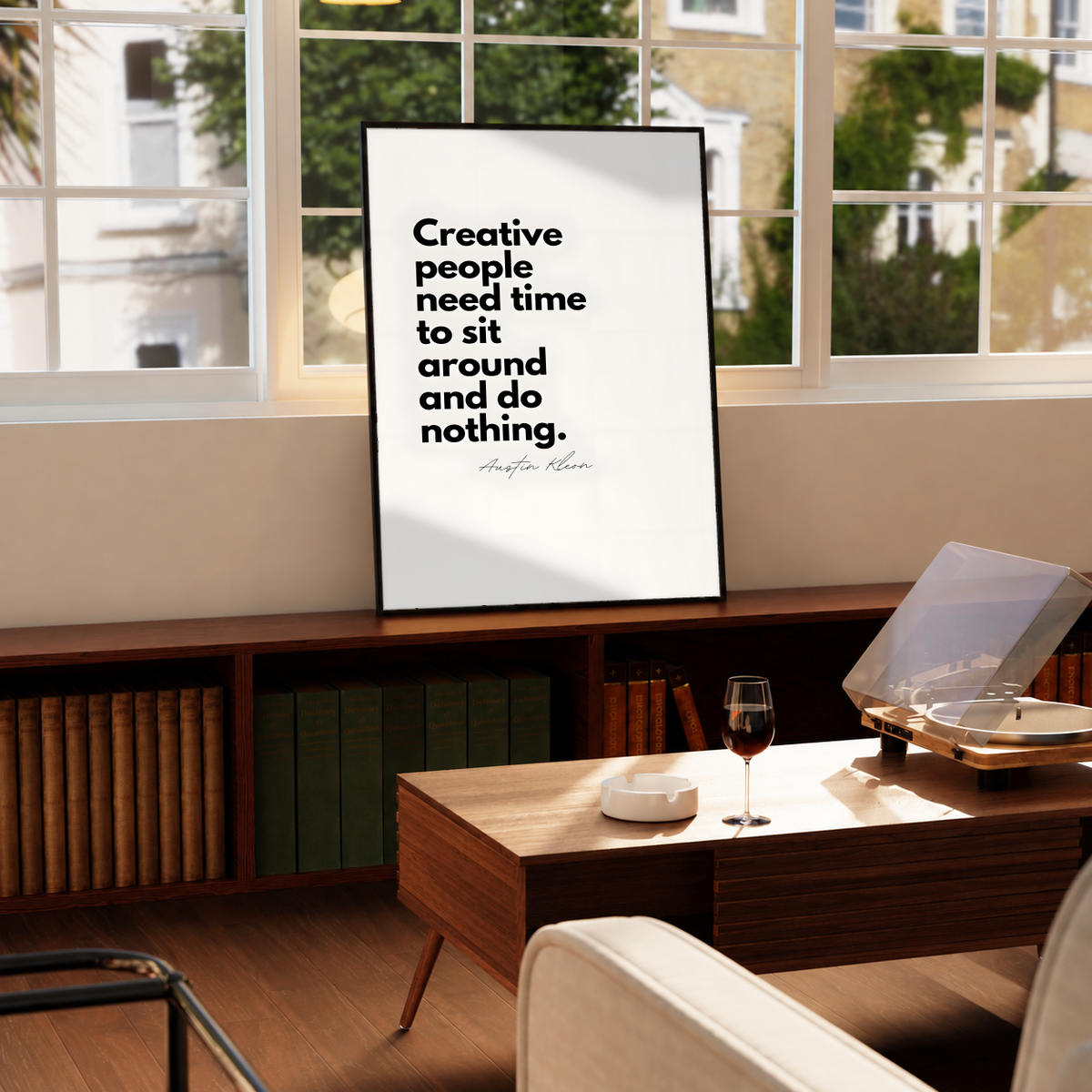 Creative people need time to sit around and do nothing quote in bold black type on cream, styled in a black frame above a wood console with books and a record player
