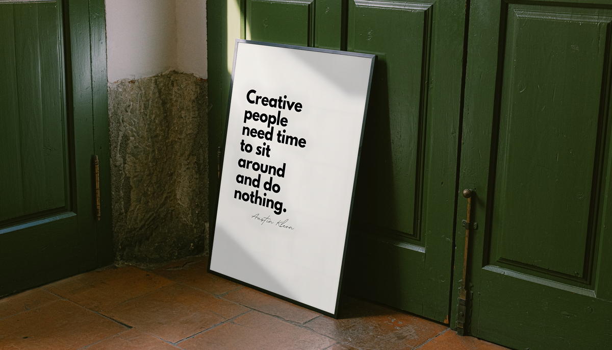 Creative people need time to sit around and do nothing quote in bold black type on cream, styled in a black frame against dark green paneled doors above orange floor tiles