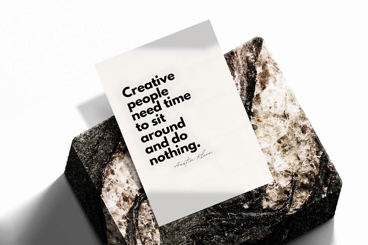 Creative people need time to sit around and do nothing quote in bold black type on cream, shown as an unframed print tilted on a dark stone display against a light background