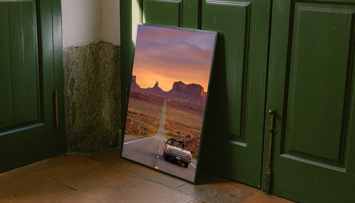 Floor-standing desert road poster with black frame near green doors
