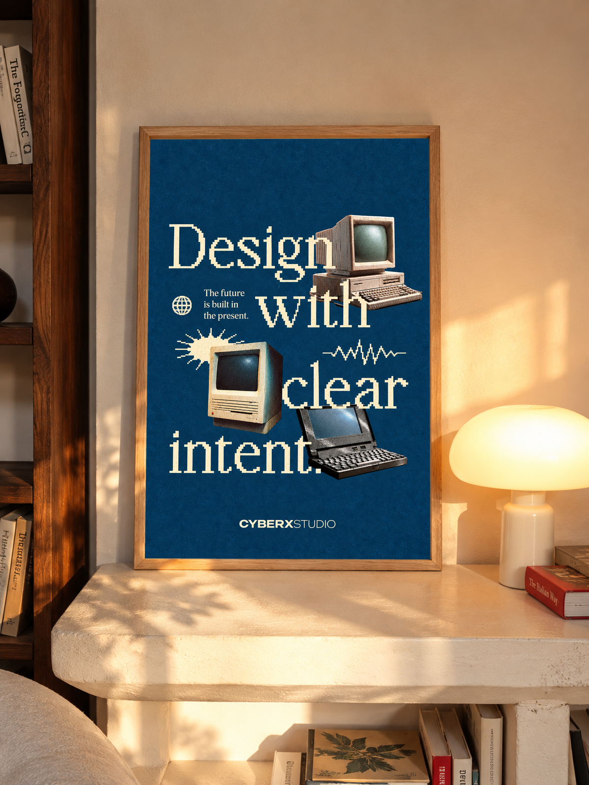 Vintage desktop computers and a laptop with cream pixel-style typography on blue in an oak frame above a pale wooden sideboard beside a glowing lamp