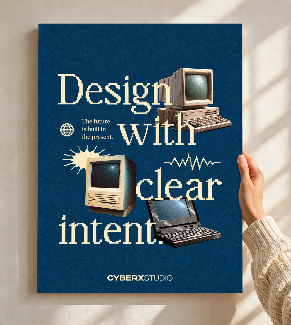 Vintage desktop computers and a laptop with cream pixel-style typography on blue as an unframed poster held against a pale sunlit wall