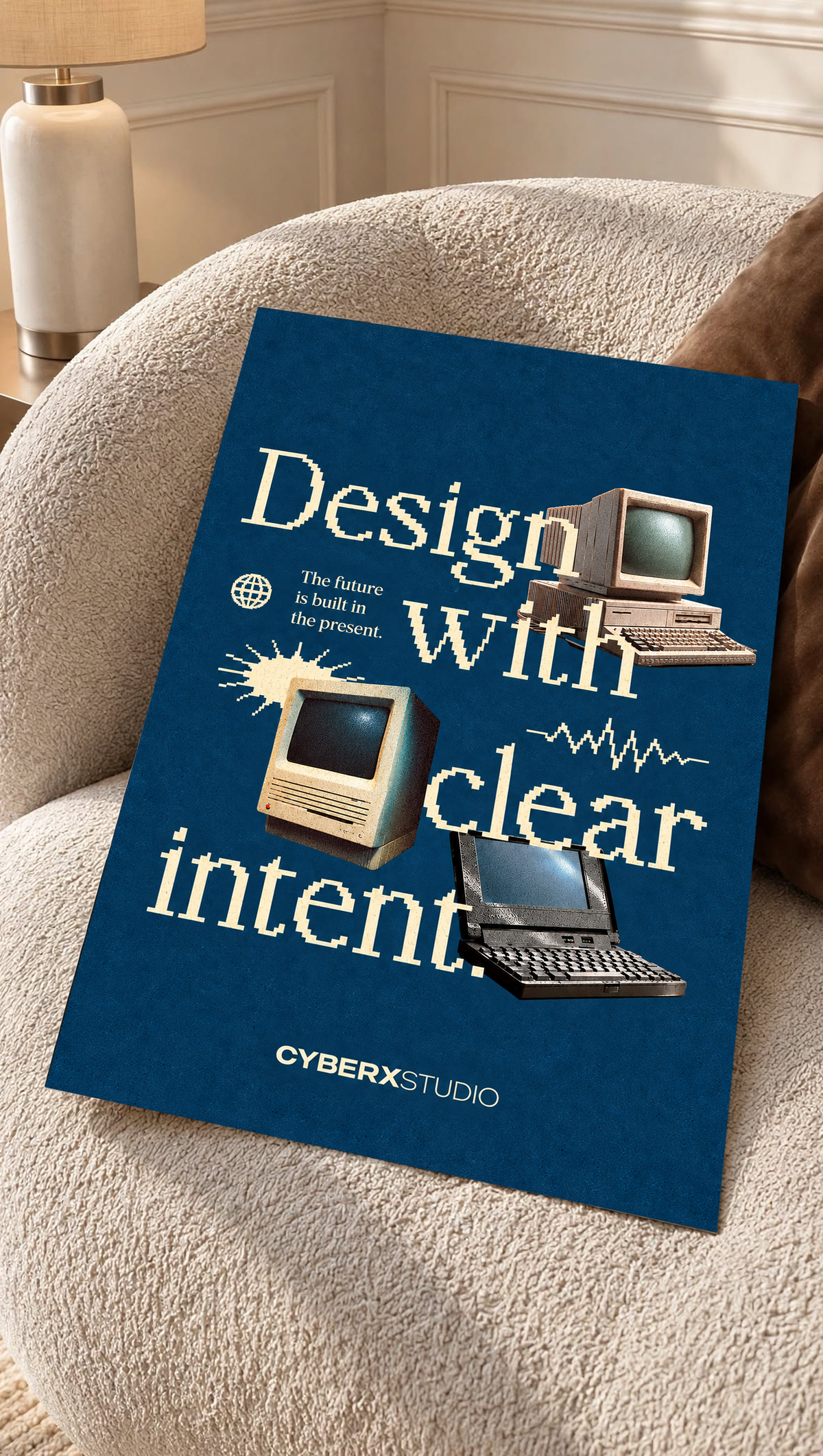 Vintage desktop computers and a laptop with cream pixel-style typography on blue as an unframed poster resting on a cream woven chair