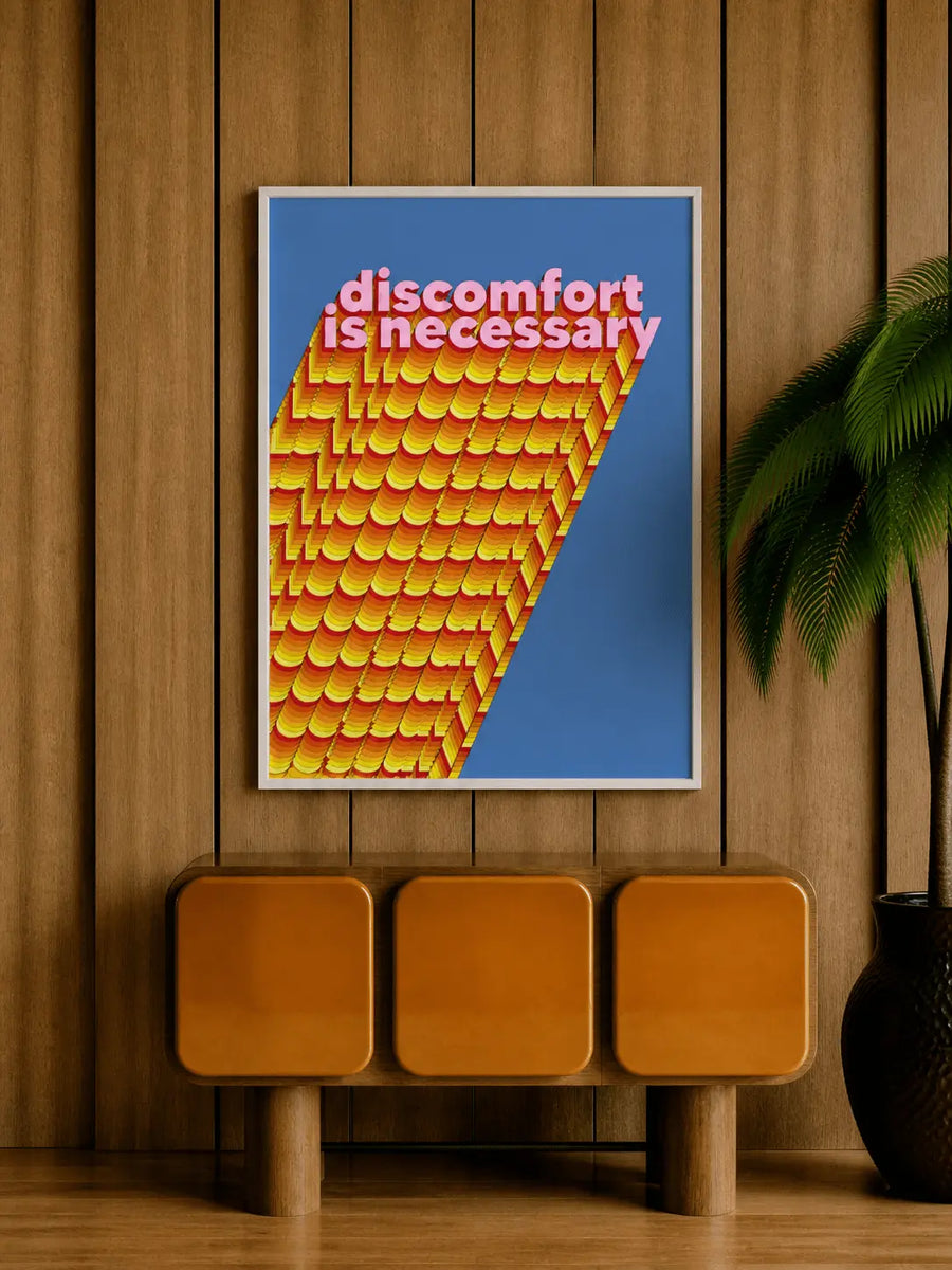 Impresión de pared con marco de roble, fondo azul y “discomfort is necessary” en rosa sobre franjas onduladas naranjas.