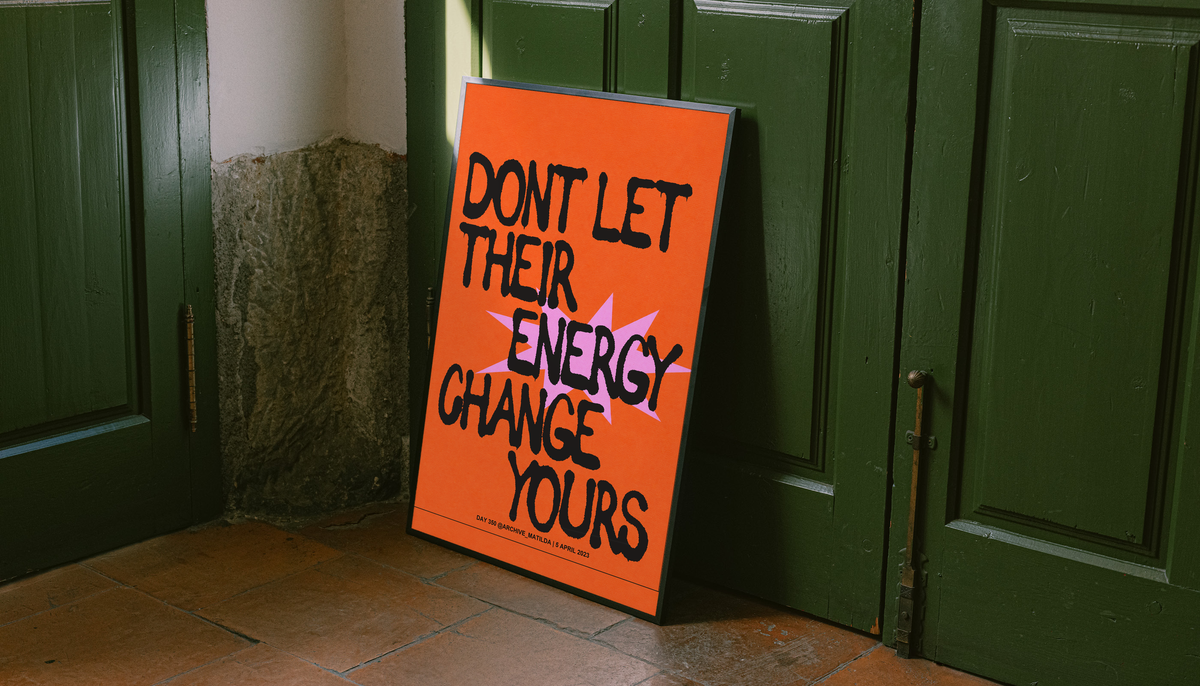 Orange poster with black border leaning near green doors, bold quote text