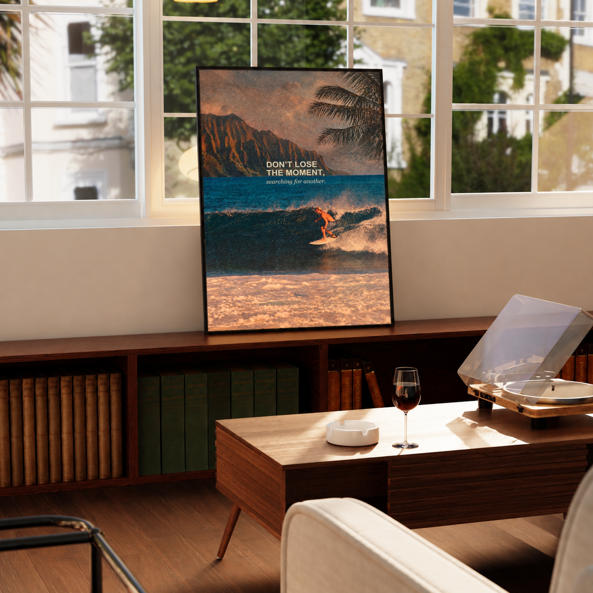 Surfer on a teal wave below warm sunset sky and palm fronds; framed print beside a window