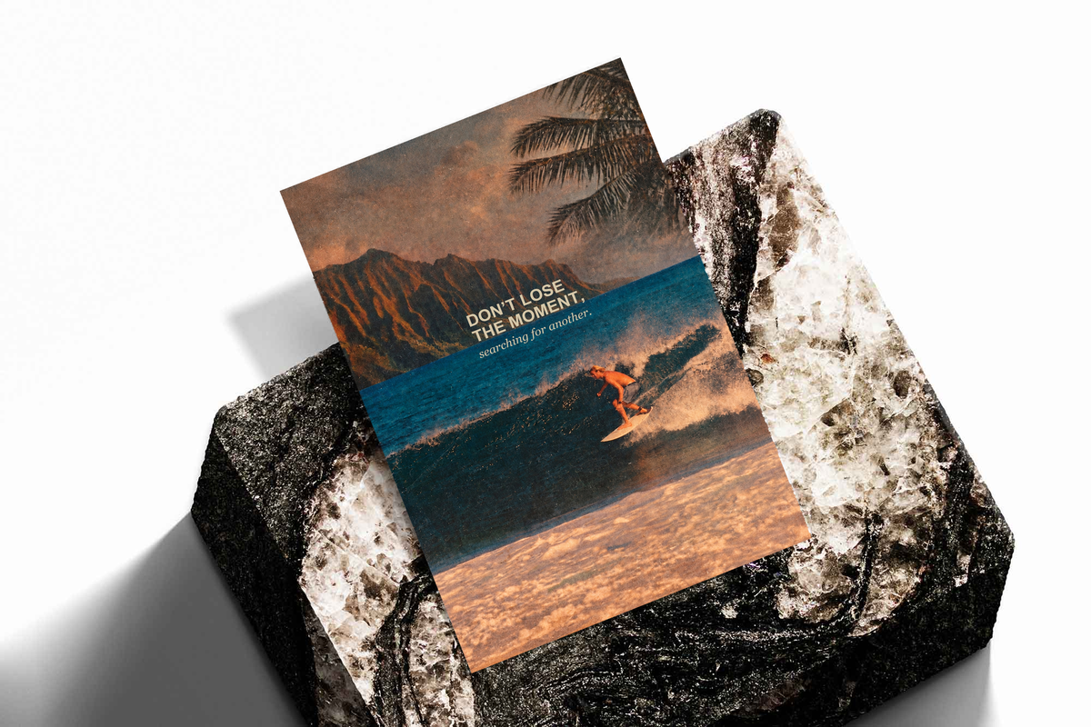 Surfer on a teal wave below warm sunset sky and palm fronds; unframed print on a stone display