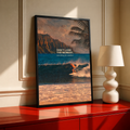 Surfer on a teal wave below warm sunset sky and palm fronds; black framed print on a red cabinet