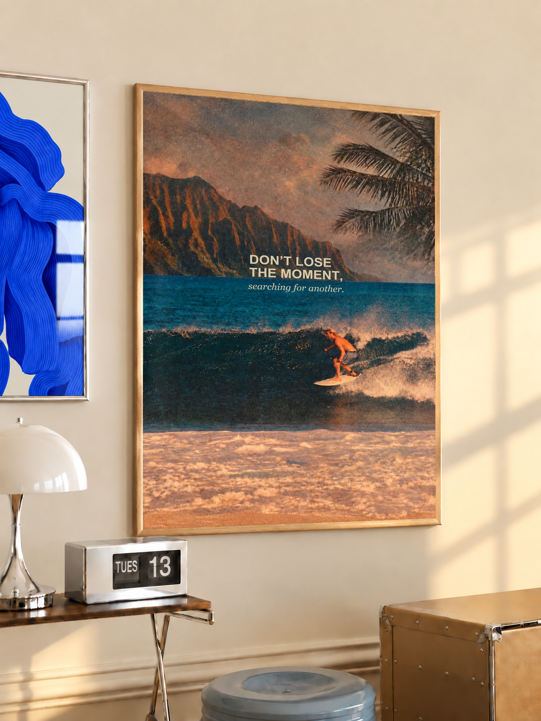 Surfer on a teal wave below warm sunset sky and palm fronds; oak framed print in a desk setting