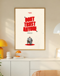 Bold red Don't Trust Anyone typography above a small seated figure on cream in a slim oak frame on a cream wall above a white cabinet