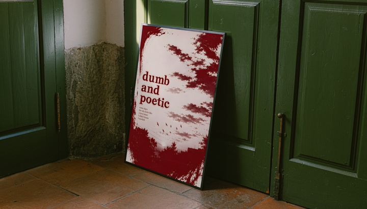 Dumb and poetic burgundy distressed lettering over pale pink clouds with birds and tree silhouettes, styled in a black frame against dark green paneled doors above orange floor tiles