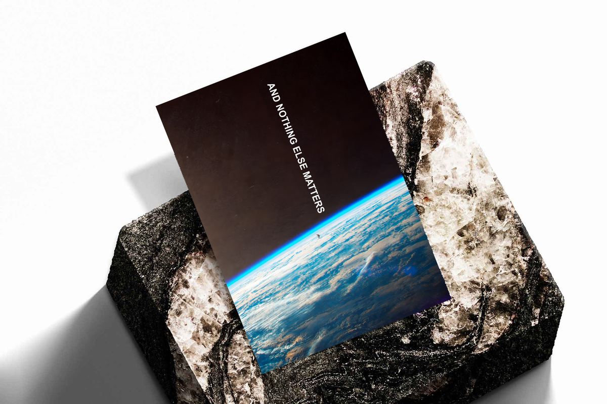 And Nothing Else Matters white vertical typography over Earth’s blue atmospheric horizon and a tiny human-shaped silhouette, shown as an unframed print tilted on a dark stone display against a light background