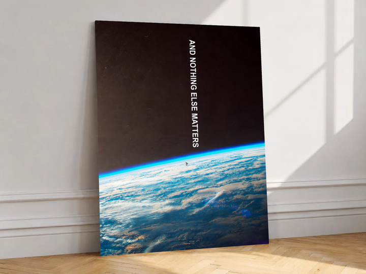 And Nothing Else Matters white vertical typography over Earth’s blue atmospheric horizon and a tiny human-shaped silhouette, shown unframed on a white wall above parquet flooring with a diagonal sun shadow