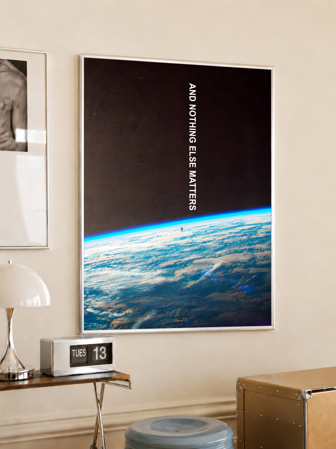 And Nothing Else Matters white vertical typography over Earth’s blue atmospheric horizon and a tiny human-shaped silhouette, styled in a light frame on a cream wall beside a white dome lamp and glass side table