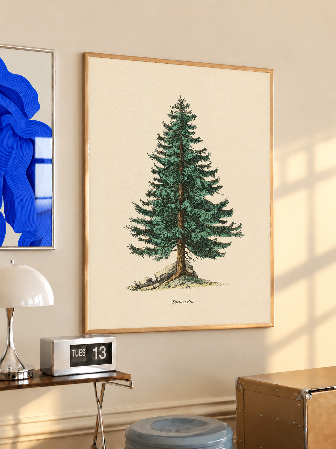Single green evergreen tree on cream with a printed Spruce Pine caption in an oak frame above a console beside a blue print and calendar
