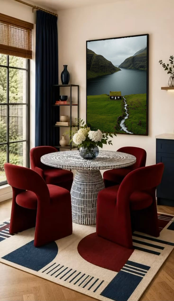 A small turf-roof cottage beside a stream overlooking a mountain-lined fjord in a black frame on the wall of a dining nook with red chairs