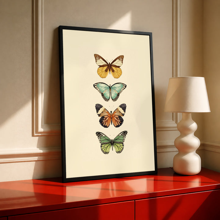 Four-butterfly illustration print in black frame on warm cream background, gold and green tones