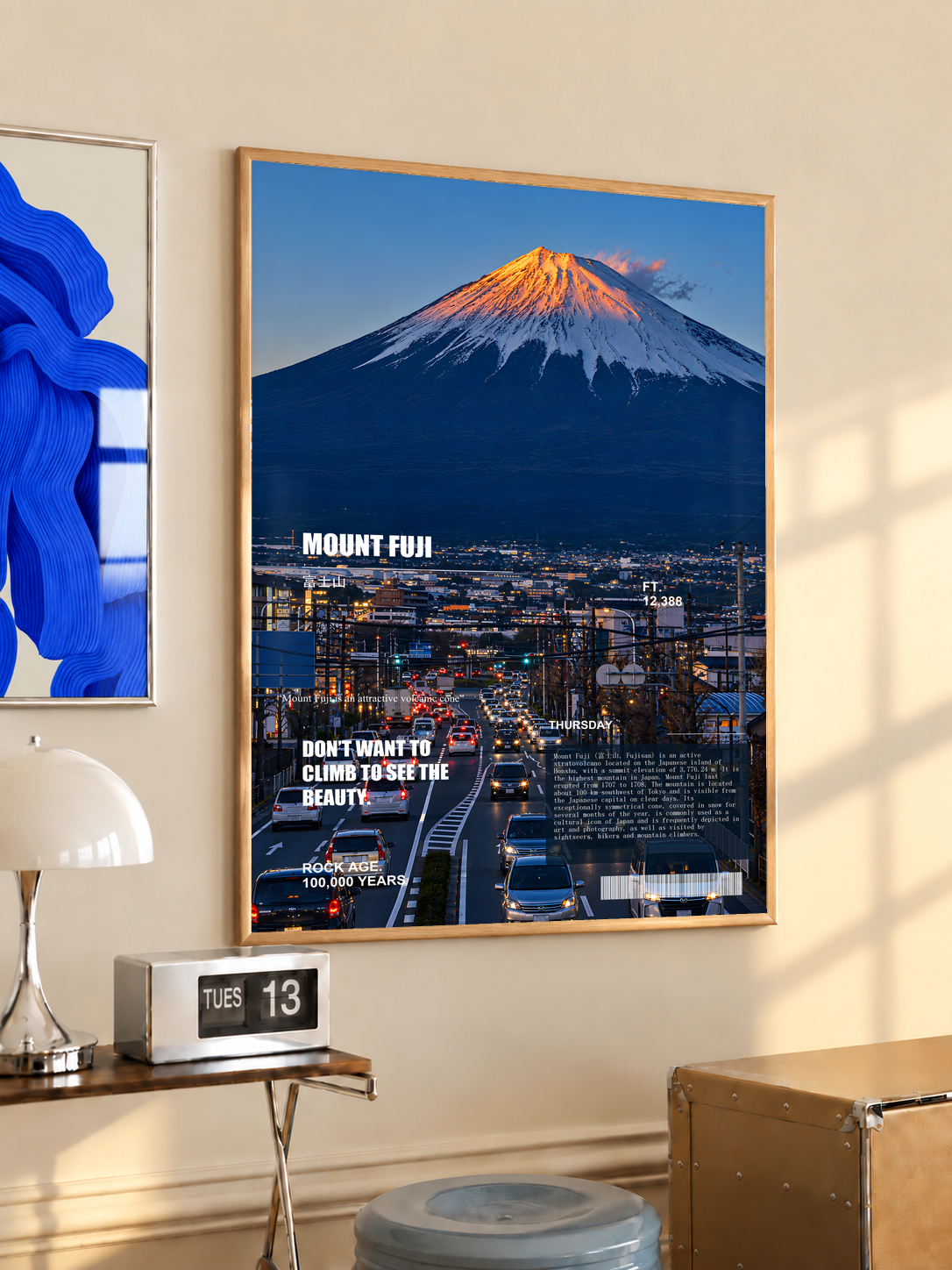 Orange-lit Mount Fuji above a deep blue city in an editorial collage; oak framed print in a desk setting