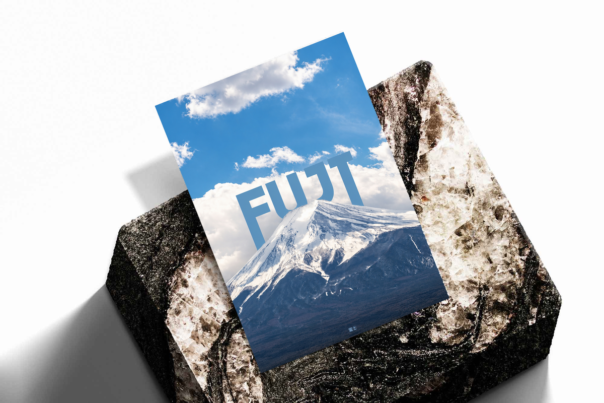 Snow-covered Mount Fuji beneath blue sky and large white FUJI lettering; unframed print on a stone display