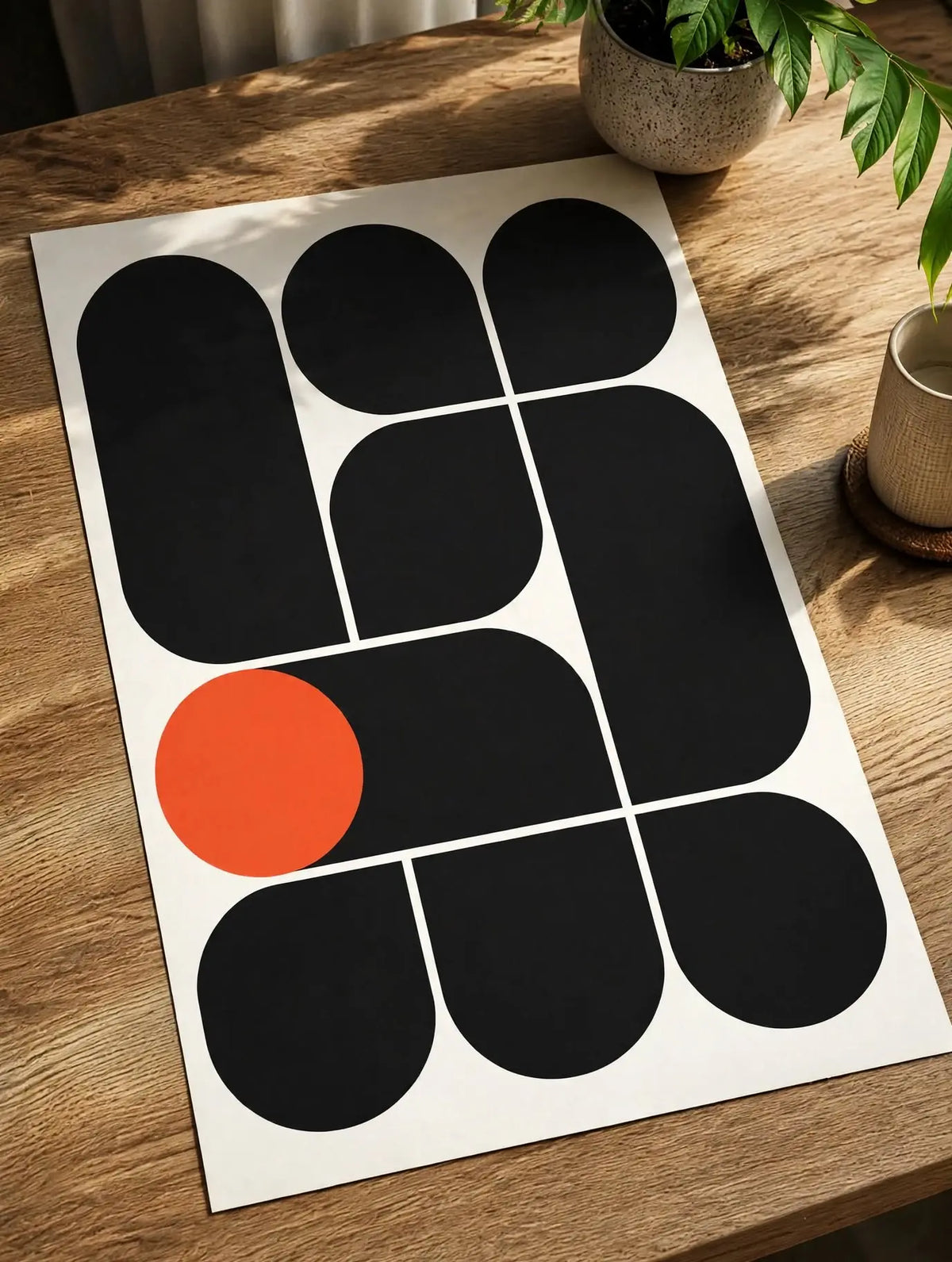 Unframed Bauhaus art print laid on wood table: black rounded shapes, white grid lines, orange dot.