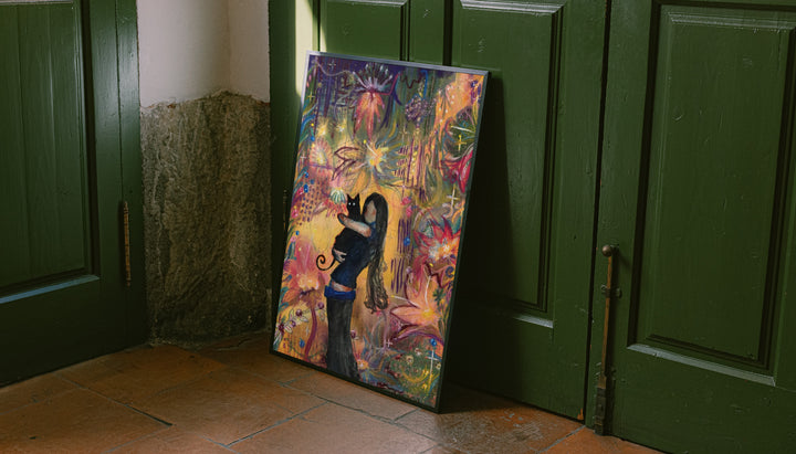 A girl embracing a black cat amid colorful ornamental flowers and patterns leaning on the floor against dark green wall panelling