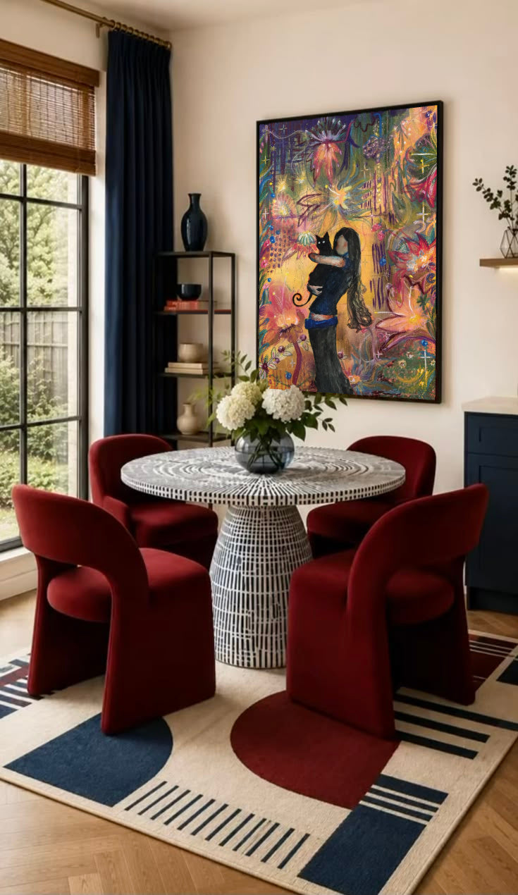 A girl embracing a black cat amid colorful ornamental flowers and patterns in a black frame on the wall of a dining nook with red chairs