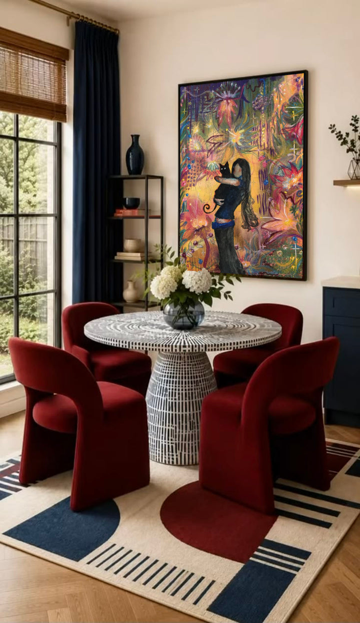 A girl embracing a black cat amid colorful ornamental flowers and patterns in a black frame on the wall of a dining nook with red chairs