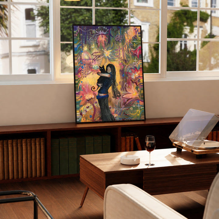 A girl embracing a black cat amid colorful ornamental flowers and patterns in a black display frame on a wooden console beside a sunlit window