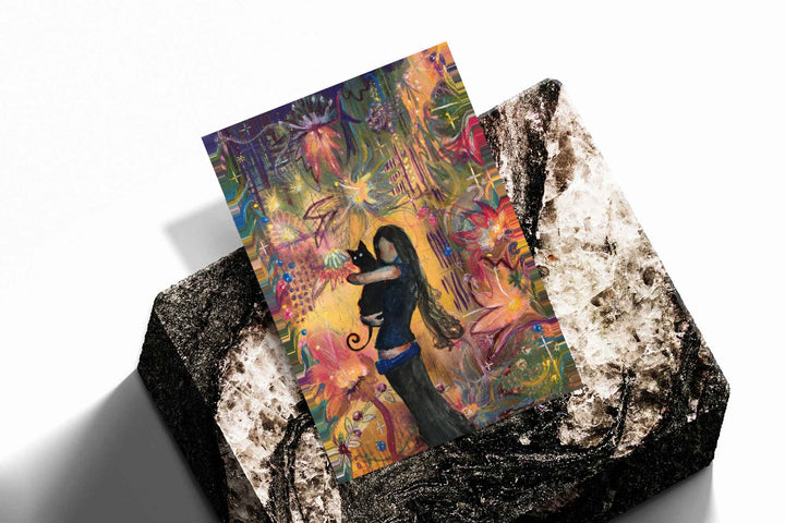 A girl embracing a black cat amid colorful ornamental flowers and patterns as an unframed print resting at an angle on a dark stone display
