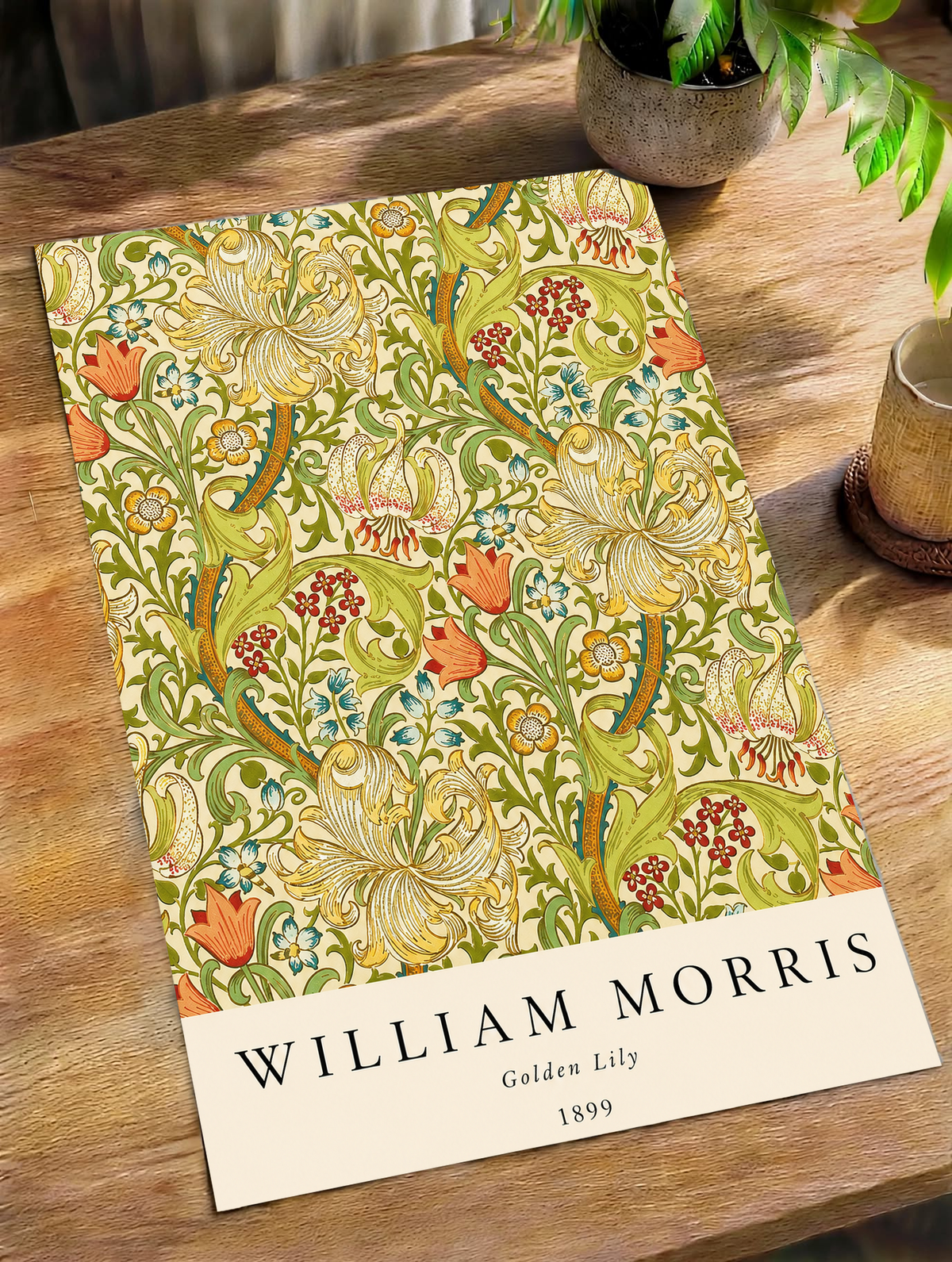 Golden Lily floral pattern with olive leaves, yellow flowers and red accents as an unframed print on a wooden table beside a plant