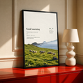 White sheep in a green pasture with misty cliffs and Good Morning lettering; black framed print on a red cabinet