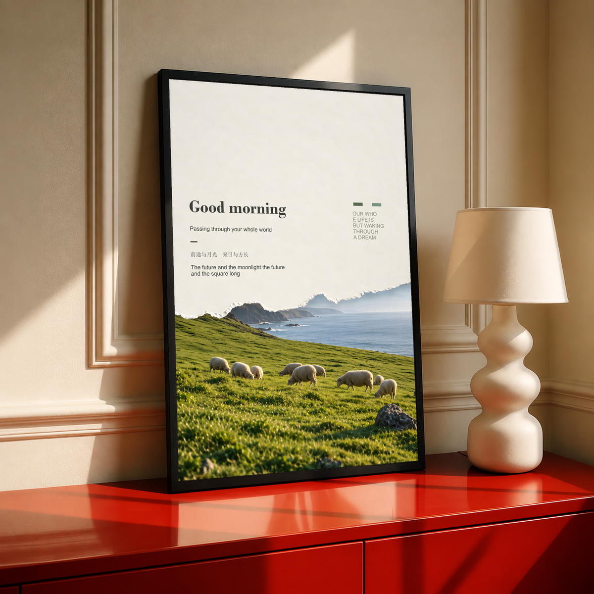 White sheep in a green pasture with misty cliffs and Good Morning lettering; black framed print on a red cabinet
