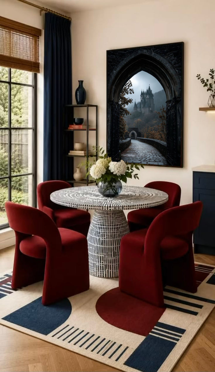 A distant gothic castle seen through a pointed stone arch above a cobbled path in a black frame on the wall of a dining nook with red chairs