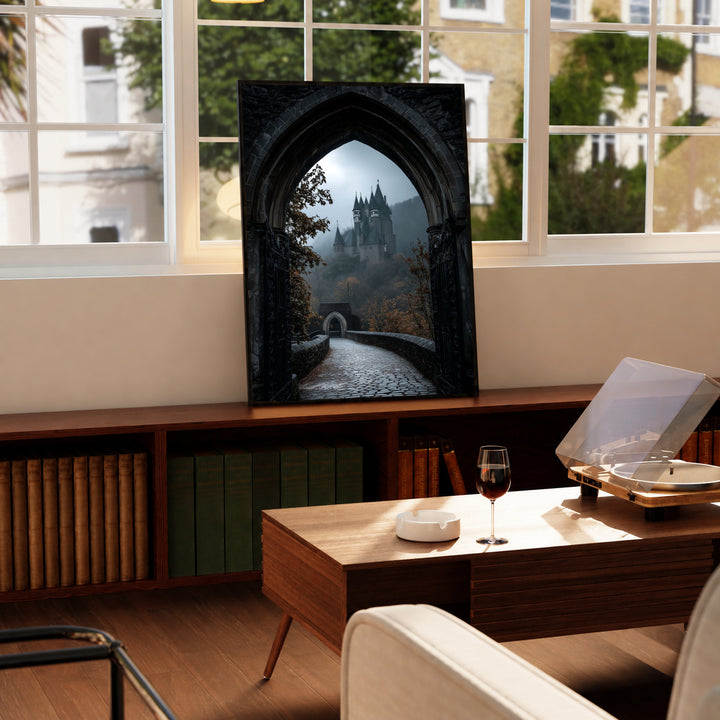 A distant gothic castle seen through a pointed stone arch above a cobbled path in a black display frame on a wooden console beside a sunlit window