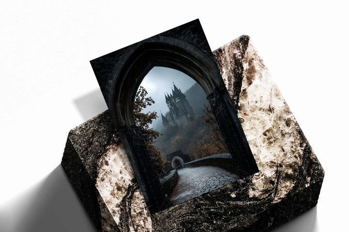 A distant gothic castle seen through a pointed stone arch above a cobbled path as an unframed print resting at an angle on a dark stone display