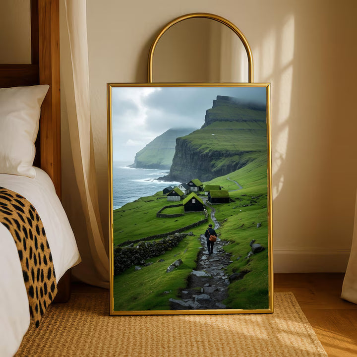 Gold-framed landscape print with green cliffs, seaside village houses, and a hiker on path