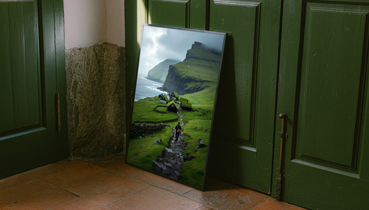 Framed landscape wall art with green cliffs, village houses, and a hiker on rocky path
