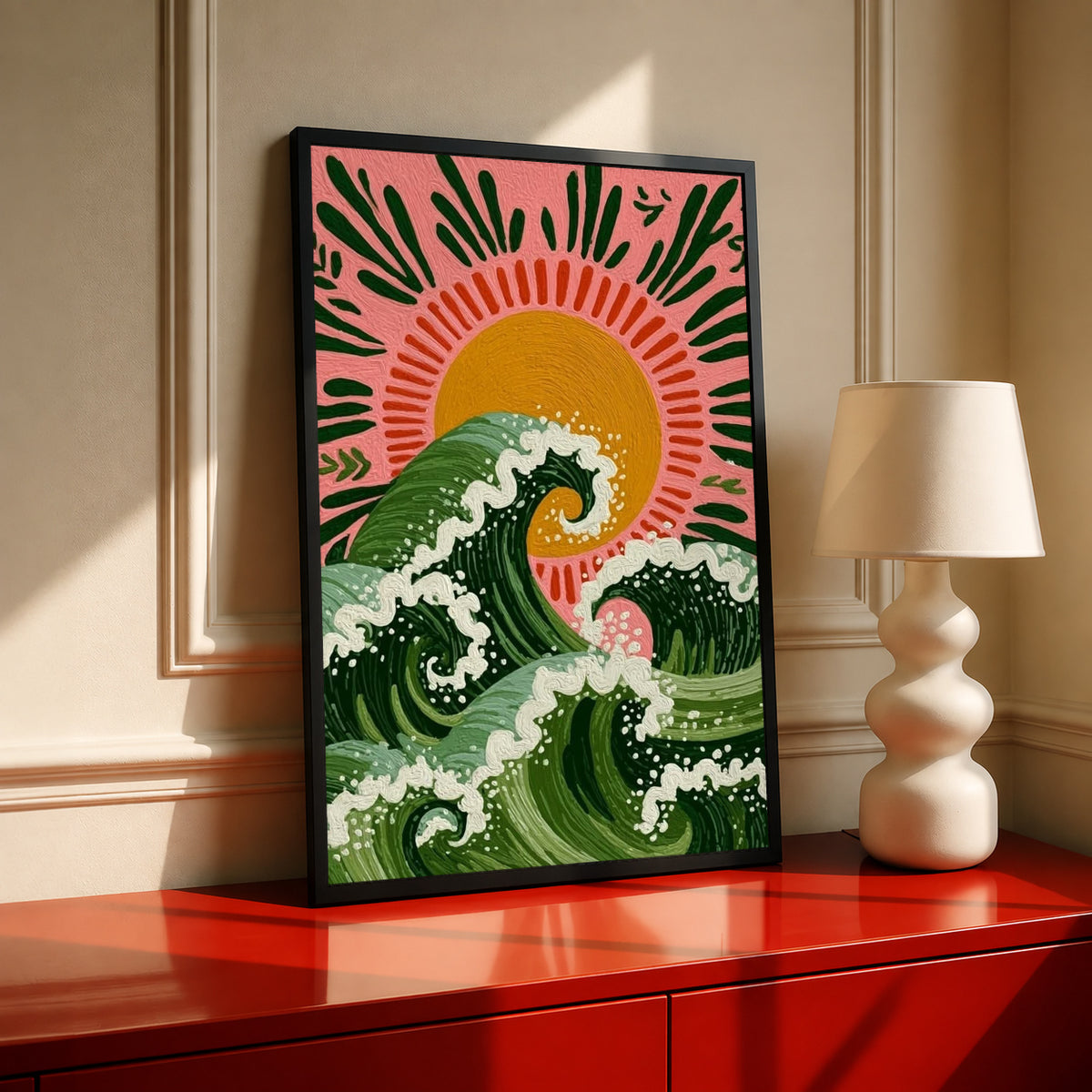 Curling green waves with cream foam beneath an orange sun on a pink background in a black frame on a red console beside a sculptural cream lamp