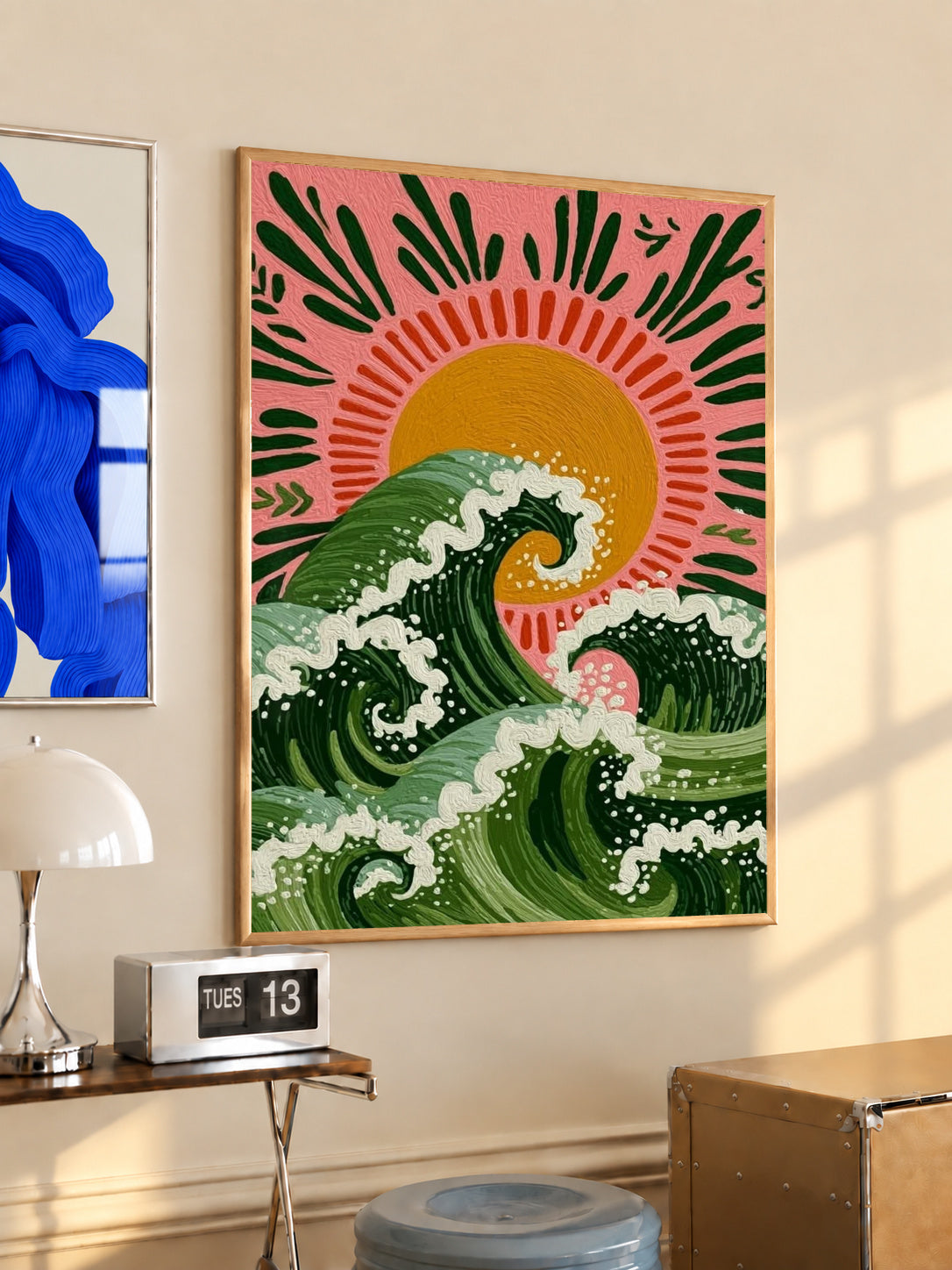 Curling green waves with cream foam beneath an orange sun on a pink background in a light wood frame on a sunlit office wall beside a desk