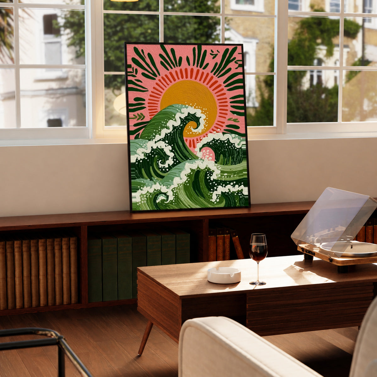 Curling green waves with cream foam beneath an orange sun on a pink background in a black display frame on a wooden console beside a sunlit window