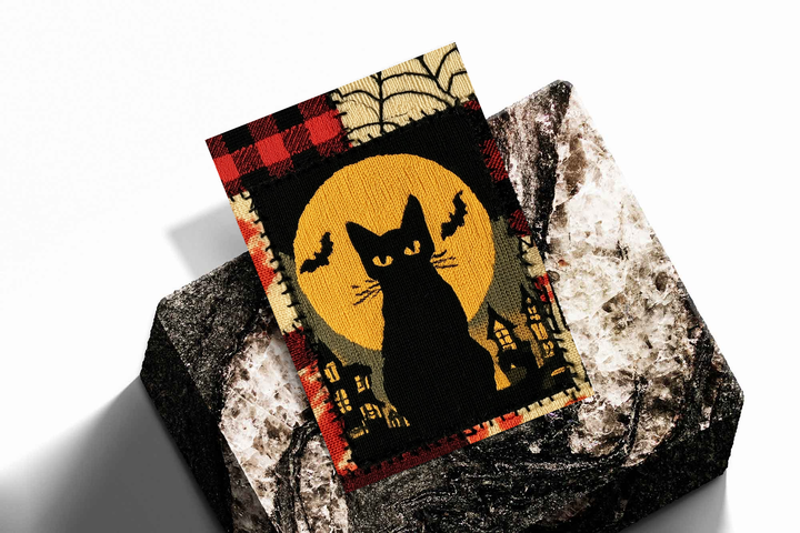 Halloween black cat and yellow moon as an unframed print propped against a pale wall on a rough stone
