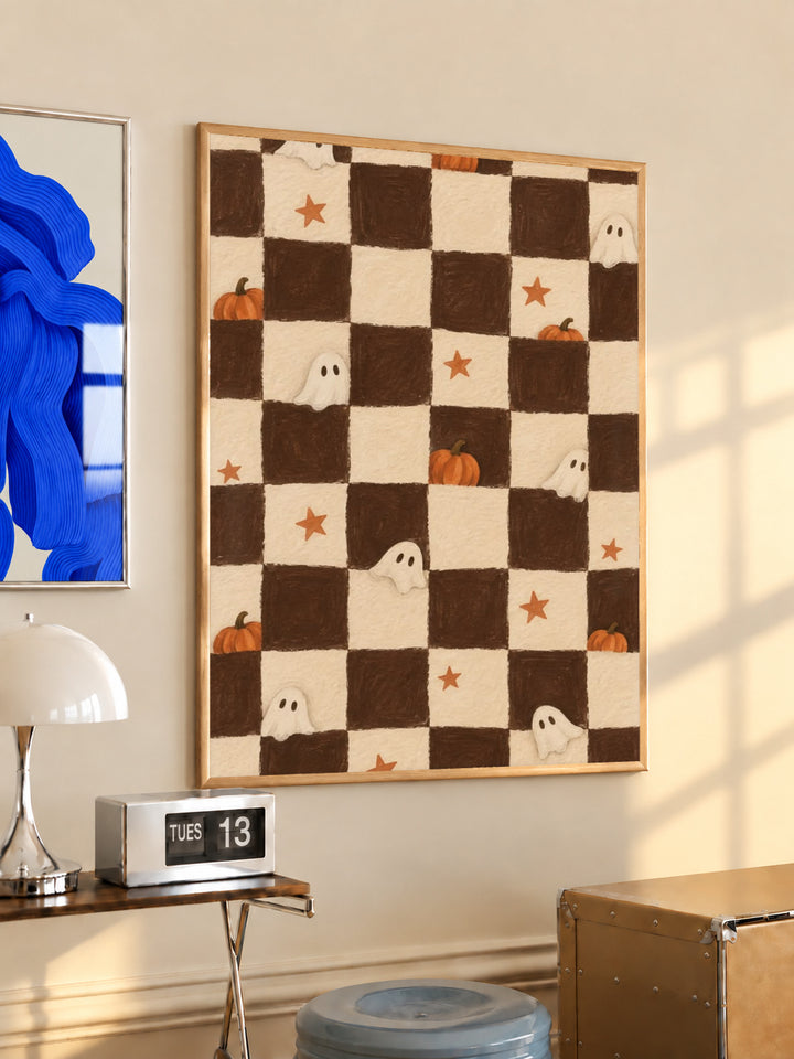Brown and cream Halloween checkerboard with little white ghosts, pumpkins and orange stars in a light wood frame on a sunlit office wall beside a desk